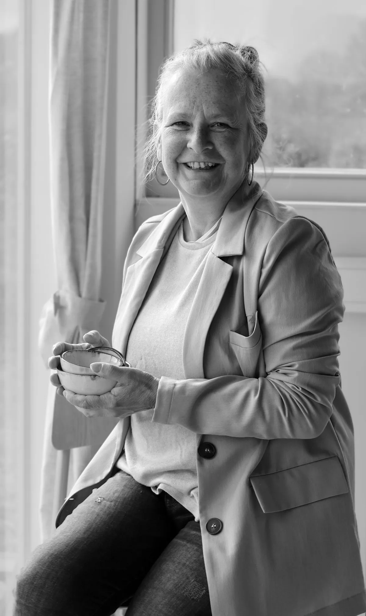 Anita Roskam zit met een kom in haar handen bij het raam