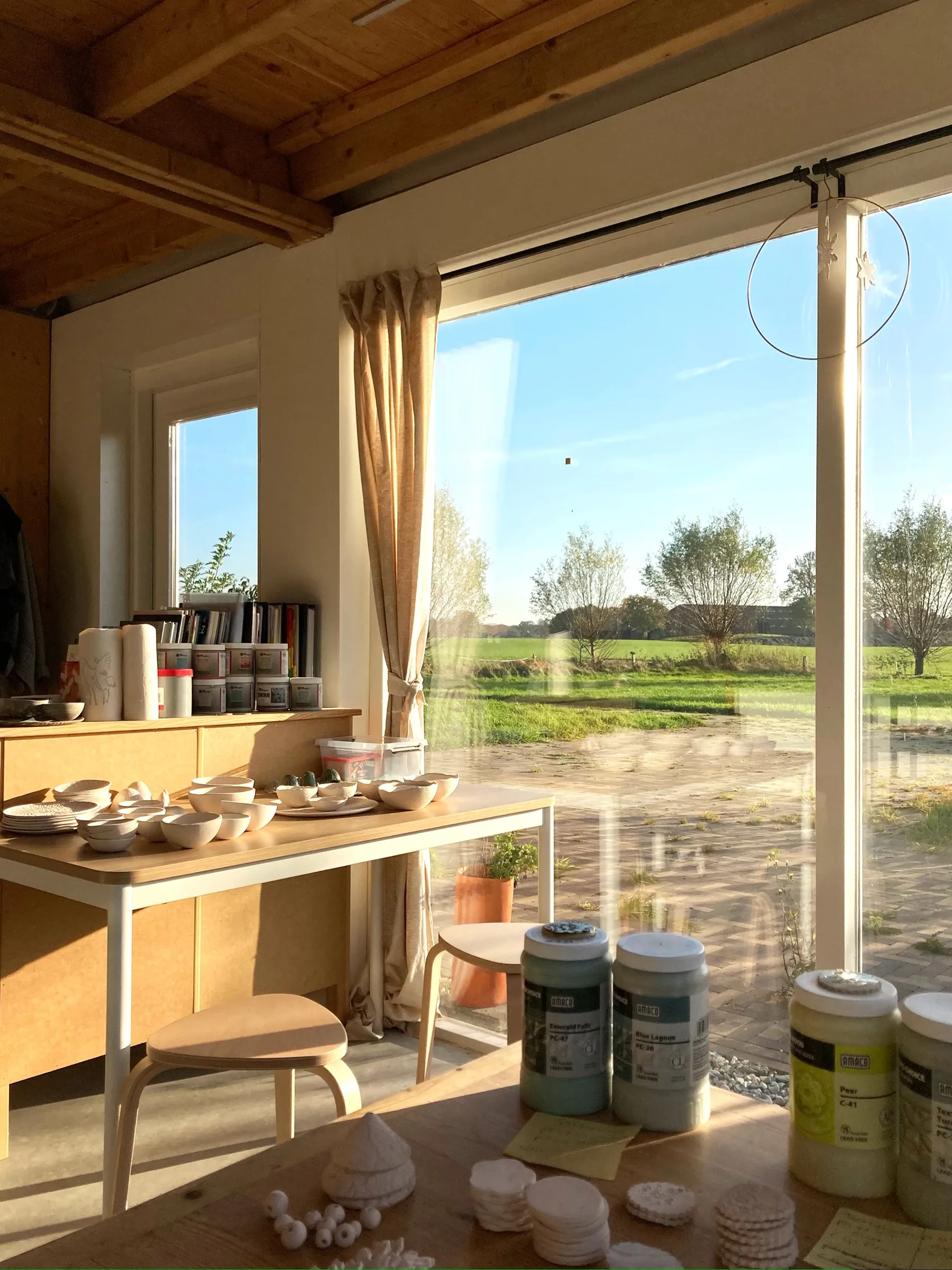 Werktafels met potten glazuur bij het grote raam