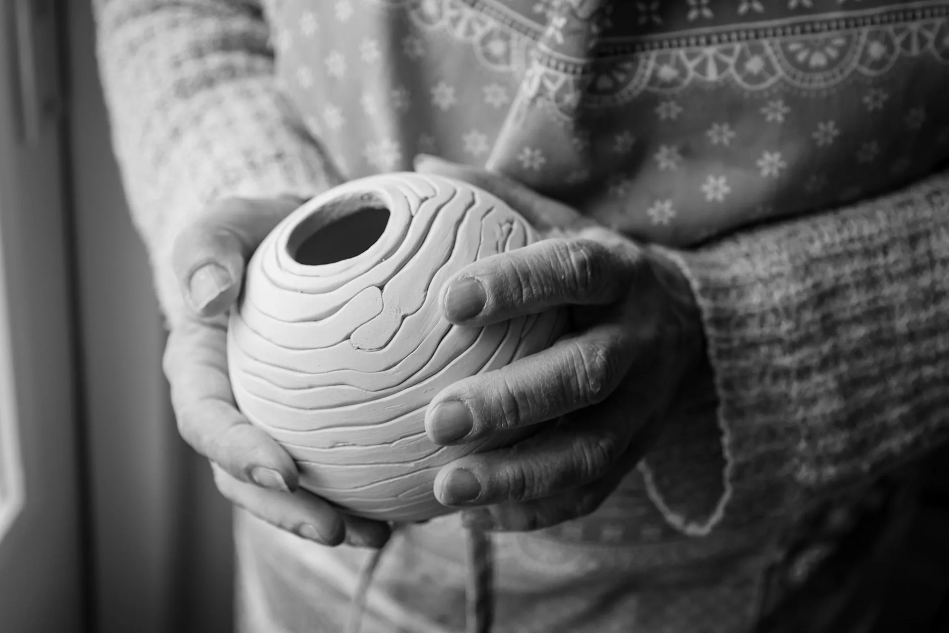 Handen houden een bolvormig kleien potje vast